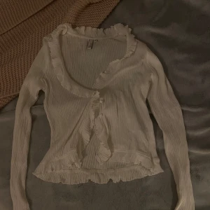 Vit ribbad kofta med volangdetaljer - Söt vit ribbad kofta med volangdetaljer längs kanterna och pärlknappar framtill. Den har ett pyttelitet hål längst ut på vänstra ärmen, men annars är den som ny 💓💓 den är knappt använd då den är lite liten för mig💓🎀 Den är i storlek M, men jag skulle säga att den är mer xs-s 💓 Hör av er om ni undrar något!! 💓                       ⚠️Använd inte Köp Nu💞💞