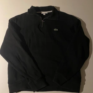 Svart tröja från Lacoste - Säljer en stilren svart tröja från Lacoste med dragkedja vid halsen och det klassiska krokodilmärket på bröstet. Tröjan har sidofickor. Bra skick, passar både M och S