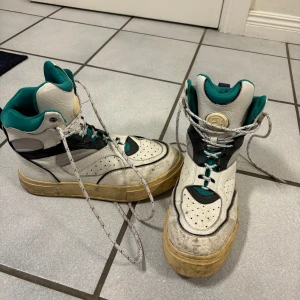 Eytys sneaker  - Säljer ett par höga sneakers i vitt med gröna och svarta detaljer. Skorna har snörning och en robust sula. Perfekta för en sportig look.