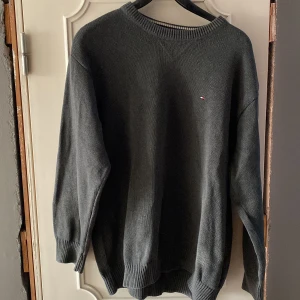 Grå stickad tröja från Tommy Hilfiger - Säljer en stilren grå stickad tröja från Tommy Hilfiger. Tröjan har en liten broderad logotyp på bröstet och ribbade muddar vid ärmslut och nederkant. Perfekt för kyligare dagar. Passar som en Large storlek!