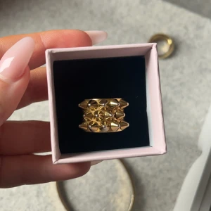 Guldfärgad ring med geometriskt mönster - Snygg guldfärgad ring med ett unikt geometriskt mönster. Ringen har en bred design som ger ett statement-utseende och passar perfekt för att lyfta vilken outfit som helst. Perfekt för dig som älskar att sticka ut med dina accessoarer.