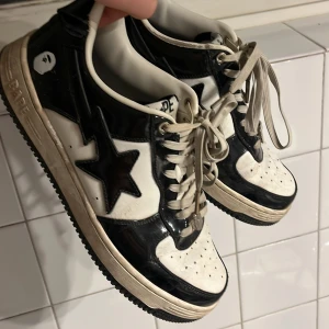 Svartvita sneakers från BAPE - Säljer ett par klassiska BAPE STA sneakers i svart och vitt. Skorna har en ikonisk stjärndetalj på sidan och snörning framtill. Perfekta för dig som gillar streetwear och vill ha en unik stil. Har trönatt på de, köpte de för ungefär 2 år sedan.