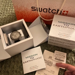 Omega x Swatch Mission to Earthphase klocka - Säljer en Swatch Mission to Earthphase klocka från Bioceramic Moonswatch Collection. Klockan har en stilren design med en vit urtavla och svarta detaljer. Helt ny model med rörelse som man ser i klockan, Den kommer i originalförpackning med tillhörande dokumentation. Perfekt för den som gillar unika och moderna klockor. Ny insläppt Omega Swatch klocka. Inköpt i Oslo och fårs med kvitto.