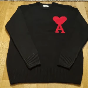 Svart tröja med rött hjärta från Ami - Snygg svart tröja från Ami Alexandre Mattiussi med ett rött hjärta och bokstaven 'A' på bröstet. Storlek S (ärm:55 cm, kropp: 65 cm). Perfekt för en stilren garderob
