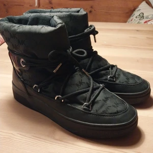 Svarta boots från Michael Kors - Snygga svarta boots från Michael Kors med logotypmönster och snörning. De har en hög design med vadderad insida för extra komfort. Perfekta för kyligare dagar.