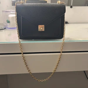 Svart axelväska med guldkedja - Säljer en svart väska med guld detaljer som är i normal storlek aldrig använd och är i bra skick 