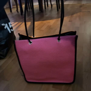 Rosa och orange shoppingväska samt svart axelväska - Säljer en färgglad shoppingväska med texten 'PARIS' i orange och rosa, samt en stilren svart axelväska med kedjerem och metallspänne. Shoppingväskan har långa handtag och är rymlig, perfekt för en dag på stan. Axelväskan är elegant och passar för en kväll ute.
