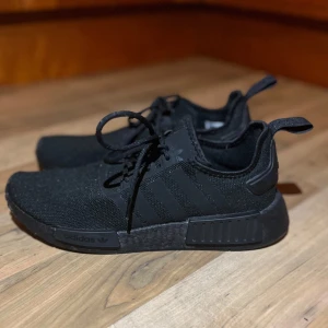 Svarta Adidas NMD sneakers - Säljer ett par svarta Adidas NMD sneakers i mycket bra skick eftersom dom inte passar, helt oanvända köpta för 1299kr. Säljer för 900 kom gärna med ett rimligt pris😊 