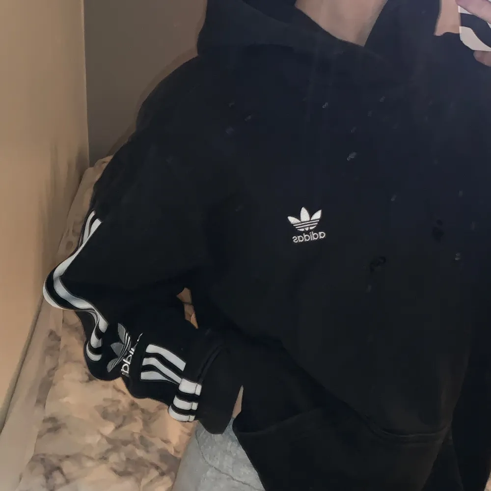 Säljer en svart hoodie från Adidas med den klassiska loggan på bröstet och de ikoniska tre ränderna längs ärmarna. Den är i bra skick och superbekväm. . Hoodies.