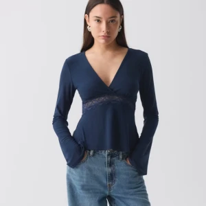 Mörkblå topp med spetsdetaljer - Snygg mörkblå topp med v-ringning och spetsdetaljer under bysten. Långärmad design som passar perfekt för både vardag och festliga tillfällen. Tillverkad i ett mjukt och bekvämt material.