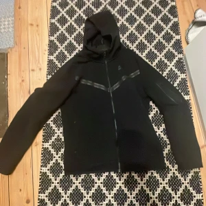 Svart fleecejacka från Nike - Säljer en svart fleecejacka från Nike i storlek XL. Jackan har en dragkedja framtill och en huva för extra värme. Perfekt för kyliga dagar och passar bra till både vardag och träning. Pris kan diskuteras.