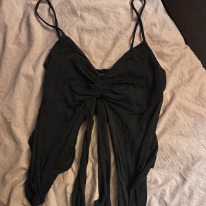 Svart ärmlös topp - Betalas via swish! Snygg svart ärmlös topp med smala axelband och knytning framtill. Perfekt för en utekväll eller fest. Materialet känns mjukt och bekvämt, och designen ger en smickrande passform. Ett måste i garderoben för alla som älskar stilrena plagg!