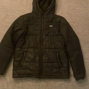 Svart quiltad jacka från Vans - Säljer en svart quiltad jacka från Vans i barnstorlek L. Den har en dragkedja framtill och en mysig huva. Perfekt för höst och vinter med sin varma och stilrena design. Jackan är i mycket bra skick och redo för nya äventyr!