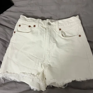 Vita jeansshorts från Zara - Säljer ett par vita jeansshorts från Zara med hög midja och fransiga kanter. Perfekta för sommardagar och festivaler. De har klassiska fem fickor och knappgylf. Supertrendiga och lätta att matcha med allt! 🌟