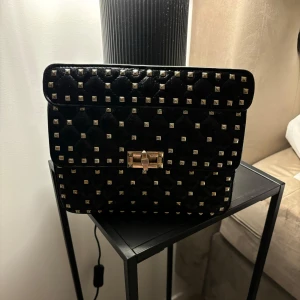 Valentino liknade väska  - Säljer nu min valentino liknande väska då den ej kommer till användning mer. Vet tyvärr inte om den är äkta då den är köpt begagnad. Har ej något kvitto. Väskans kedja är rostig som syns på bilden och lite sliten vid handtaget som visas på bilden.