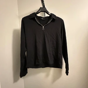 Svart tröja med dragkedja - En stilren svart tröja med dragkedja i kragen från New Yorker i storlek L. Perfekt för både vardag och fest. Tröjan har långa ärmar och en normal passform. Materialet känns mjukt och bekvämt. Oanvänd!