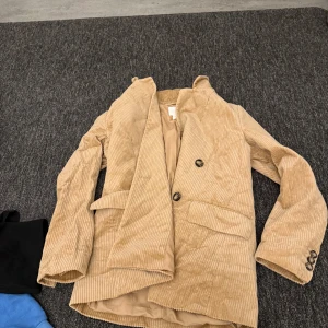 Beige manchesterkavaj från H&M - Säljer en snygg beige manchesterkavaj från H&M. Kavajen har en klassisk design med två knappar framtill och långa ärmar. Perfekt för en stilren look.