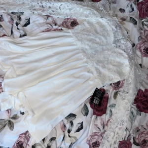 Vit spets playsuit  - Säljer en superfin vit playsuit med spetsdetaljer. Den har en vacker spetsöverdel och en flödande kjol. Perfekt för sommarens fester eller kanske till studenten. Playsuit är axelbandslös och har en romantisk känsla. Passar perfekt för en elegant look!