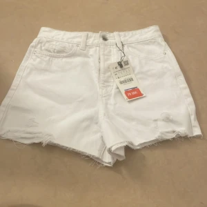 Vita jeansshorts från Zara - Säljer ett par vita jeansshorts från Zara med fransiga kanter. Perfekta för sommardagar och festivaler. Högmidjade och bekväma med en avslappnad passform.