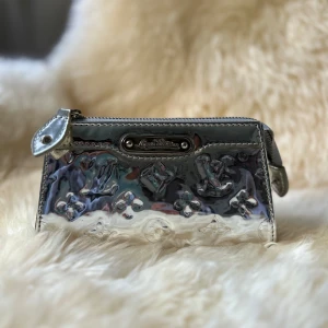 Silverfärgad plånbok från Louis Vuitton - Snygg och glansig silverfärgad plånbok från Louis Vuitton med präglat mönster och dragkedja. Perfekt för att hålla dina kort och kontanter säkra med stil. Den har en elegant design som passar både till vardags och fest.
