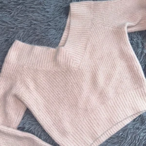 Rosa stickad tröja - Mysig beige stickad tröja med ribbad struktur. Perfekt för kyliga dagar och ger en stilren look. Tröjan har en v-ringad design både fram och bak och långa ärmar, vilket gör den både bekväm och trendig. 
