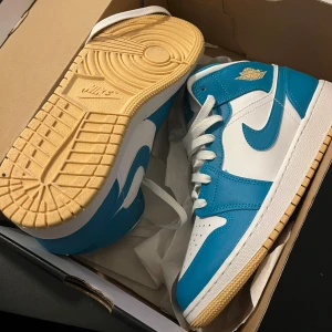 Nike Air Jordans i blått och vitt storlek 39 - Snygga Nike Air Jordans i en fräsch blå och vit färgkombination. Skorna har en klassisk design med snörning och en guldfärgad logotyp på sidan. Perfekta för dig som vill ha en stilren och sportig look. Aldrig använda! 