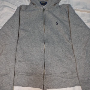 Grå hoodie från Polo Ralph Lauren - Säljer en grå hoodie från Polo Ralph Lauren i storlek 10-12 år. Den har en dragkedja framtill. Går att diskutera priset.
