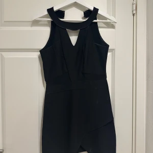 Svart ärmlös klänning med v-ringning - Elegant svart klänning med v-ringning och asymmetrisk design. Den är ärmlös och har en stilren look som passar perfekt för festliga tillfällen.