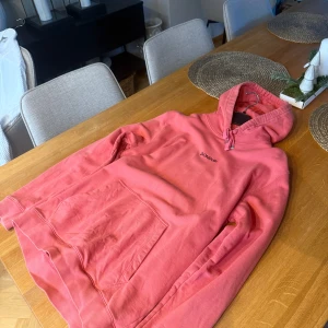 Röd hoodie från Dondup - Säljer en snygg röd hoodie från Dondup. Den har en enkel design med märkeslogga på bröstet. Säljes då den sitter lite för stort på mig. Tröjans färg upplevs som lite rödrosa. Made in Italy och gjord i 100% bomull