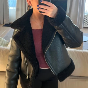Svart skinnjacka med foder - Säljer en snygg svart skinnjacka med mjukt foder. Jackan har en cool dragkedja och är perfekt för höst och vinter. Den är långärmad och har en stilren look som passar till allt. Perfekt för att hålla sig varm och trendig! Ordinarie pris 999kr