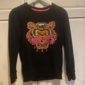 Svart sweatshirt från Kenzo - Säljer en svart sweatshirt från Kenzo med deras ikoniska tigerbroderi i färgglada nyanser på framsidan. Tröjan är i bomull och har långa ärmar. Perfekt för en casual look eller att klä upp med accessoarer. Använd men i bra skick!💗