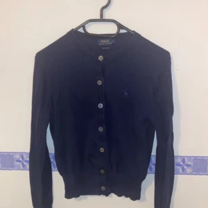 Mörkblå kofta från Polo Ralph Lauren - Säljer en snygg mörkblå kofta från Polo Ralph Lauren i pima bomull. Den har knappar hela vägen och en liten logga på bröstet. Perfekt för både vardag och lite finare tillfällen. Passar bra till höst och vår!