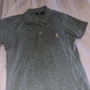 Grå piké från Ralph Lauren - Säljer en klassisk grå piké från Ralph Lauren i storlek S. Tröjan har korta ärmar och en liten broderad logga på bröstet. Perfekt för både vardag och lite finare tillfällen. Skön och stilren design!