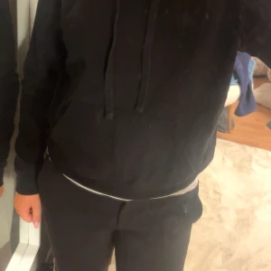 Svart hoodie - Säljer en klassisk svart hoodie med dragsko i huvan. Perfekt för en avslappnad stil och passar till det mesta. Den har långa ärmar och en bekväm passform. Orgenal pris 350.