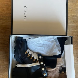 Oanvända  boots från Gucci stl 40 - Helt oanvända Snygga svarta boots från Gucci i skinn med grov sula och vita snören. Skorna har dekorativa pärlor och pälsdetaljer vid skaftet. Perfekta för en trendig look. Slutsålda överallt. Stl 40