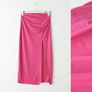 Rosa kjol med slits - Helt oanvänd! Snygg rosa kjol i ett mjukt och stretchigt material. Kjolen har en elegant slits framtill och en smickrande rynkdetalj på sidan. Perfekt för sommarens fester eller en dag på stan. Passar bra med både klackar och sneakers för en mer avslappnad look.