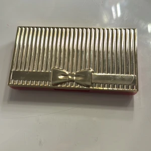 Ögonskuggspalett från Estée Lauder - Snygg ögonskuggspalett från Estée Lauder med 10 olika nyanser. Paletten har en lyxig guldig förpackning med en söt rosett på locket. Färgerna varierar från neutrala toner till djärva blå och lila nyanser, perfekt för både vardag och fest. Inkluderar en spegel för enkel applicering.