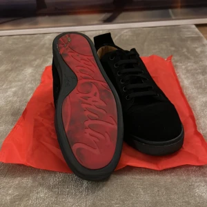 Svarta sneakers från Christian Louboutin - Säljer ett par snygga svarta sneakers från Christian Louboutin. De är i mocka med klassisk röd sula och har snörning. Perfekta för både vardag och fest! Skorna är i bra skick och kommer med originalpåse.