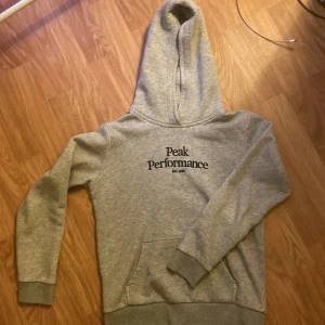 Grå hoodie från Peak Performance - Säljer en grå hoodie från Peak Performance i storlek 150. Den är supermjuk och perfekt för kyliga dagar. Hoodien har en klassisk design med en stor ficka fram och ribbade muddar vid ärmslut och nederkant. Perfekt för både vardag och träning!