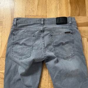 Grå jeans från Nudie Jeans - Säljer ett par snygga grå jeans från Nudie Jeans. De har en slim passform och är tillverkade i bomull. Klassisk femficksdesign med snygga sömmar på bakfickorna. Perfekta för både vardag och fest! 🕺W 31 L 32