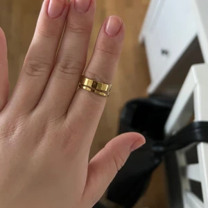 Guldfärgad ring - Snygg guldfärgad ring med en modern och stilren design. Ringen har en öppen baksida vilket gör den justerbar och bekväm att bära. Perfekt för att ge en elegant touch till vilken outfit som helst. Passar både till vardags och festliga tillfällen.