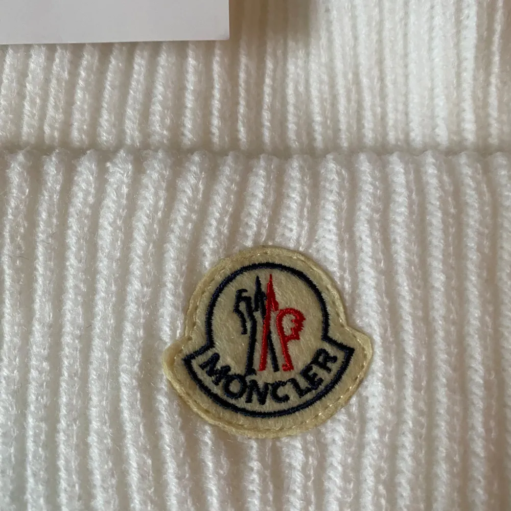 Säljer en snygg vit mössa från Moncler. Den är supermjuk och har Monclers ikoniska logga broderad framtill. Perfekt för att hålla sig varm och stilren under vintern. Mössan är i nyskick och kommer med originaltaggar. Passar perfekt till både vardag och fest!. Accessoarer.