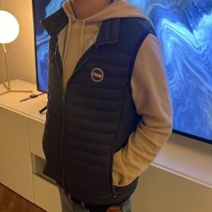 Mörkblå dunväst från colmar - Säljer en snygg svart dunväst från Colmar i mycket bra skick. Västen har en dragkedja framtill och är perfekt för höst och vår. Den är quiltad och har en normal passform, vilket gör den både stilren och bekväm. Perfekt för lager-på-lager-stil! I storlek 166cm/14 år