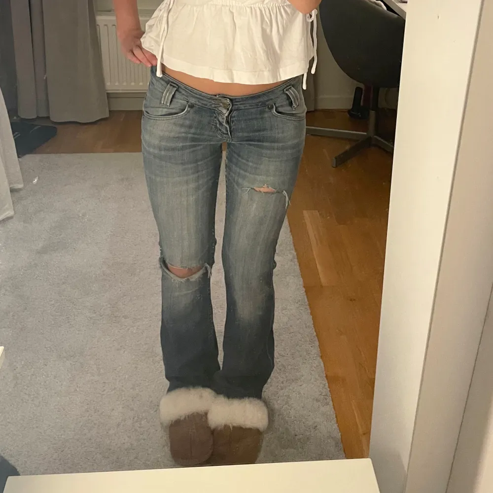 Säljer ett par snygga blå jeans från Lee med slitningar på knäna. De är lågmidjade och har en bootcut-stil som ger en avslappnad look. Perfekta för en casual outfit! 🦋. Jeans & Byxor.