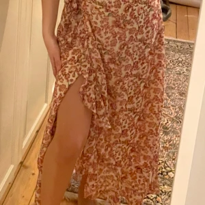 Blommig omlottkjol från Vero Moda - Säljer en superfin blommig omlottkjol från Vero Moda i storlek XS. Kjolen har en härlig slits och volangdetaljer. Perfekt för sommarens alla fester eller en mysig dag på stan. Materialet är lätt och luftigt, vilket gör den skön att bära under varma dagar. 🌸