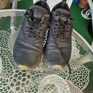 Svarta Nike sneakers - Säljer ett par svarta Nike sneakers i välanvänt skick. De har en klassisk design med snörning och en bekväm sula. Perfekta för vardagsbruk eller träning. Lite smutsiga men kan enkelt rengöras för en fräsch look.