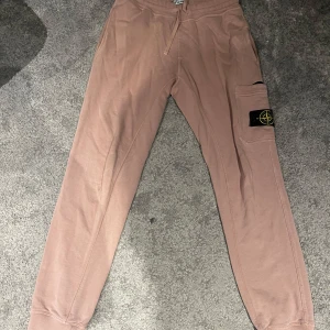 Beige mjukisbyxor från Stone Island - Säljer ett par snygga beige/ross mjukisbyxor från Stone Island. De har en bekväm passform med snörning i midjan och en cool logga på benet. Storlek S och passar S-M, 8.5/10, riktigt bra pris och är ÄKTA!
