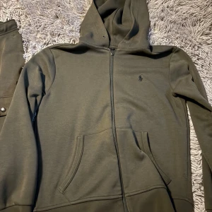 Polo Olivgröna cargopants med huva  - Säljer ett par olivgröna cargopants med matchande hoodie. Byxorna har praktiska fickor med knappar och snörning i midjan. Perfekt för en avslappnad stil eller vardagsäventyr. Hoodien har dragkedja och en liten logga på bröstet. Superbekväma och stilrena!