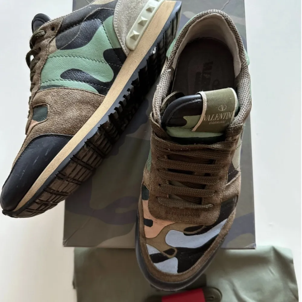 Säljer ett par snygga Valentino Garavani sneakers i camouflage. De har en cool mix av gröna, bruna och svarta nyanser med en klassisk snörning. Skorna är i mycket bra skick och kommer med originalförpackning och dustbag. Perfekta för att ge din outfit en edgy touch!. Skor.