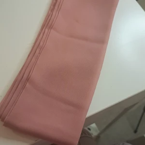 Rosa scarf från Gina Tricot - Säljer en superfin rosa scarf från Gina Tricot. Den är gjord av 100% polyester och är perfekt för att ge lite färg till din outfit. Den är mjuk och lätt, vilket gör den idealisk för både vardag och fest. Använd den som accessoar runt halsen eller knyt den på väskan för en chic look!